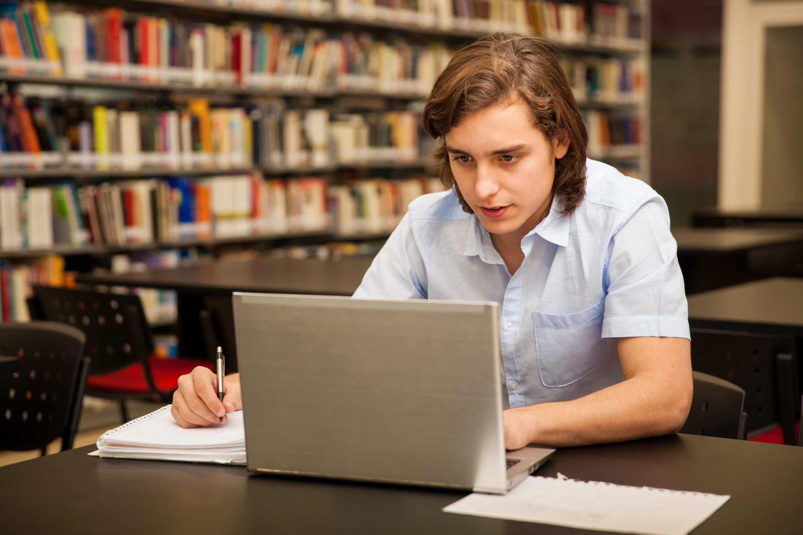 Attractive male college student using a laptop and doing some homework in the school library